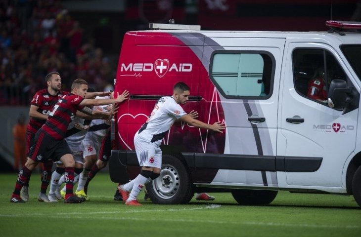 Pemain Flamengo, Everton Riberio (kiri), Piris da Motta (tengah) dan Pemain Vasco da Gama, Andrey (kanan) membantu mendorong mobil ambulans yang mogok membawa Bruno Silva yang terkena cedera pada 15 September 2018 (Pedro Martins/AFP)