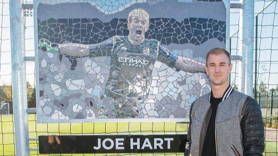 Joe Hart berdiri di depan Mozaik dan namanya yang dijadikan nama tempat latihan akademi Manchester City (@ManCity/Twitter)