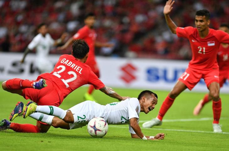 Pemain Timnas Indonesia Riko Simanjuntak (tengah) terjatuh usai berebut bola dengan pemain timnas Singapura Gabriel Quak Jun Yi (kiri) dalam penyisihan grub B Piala AFF 2018 di Stadion Nasional Singapura, Jumat (9/11/2018). Indonesia kalah 0-1 dalam pertandingan perdana tersebut. (ANTARA FOTO/Sigid Kurniawan)