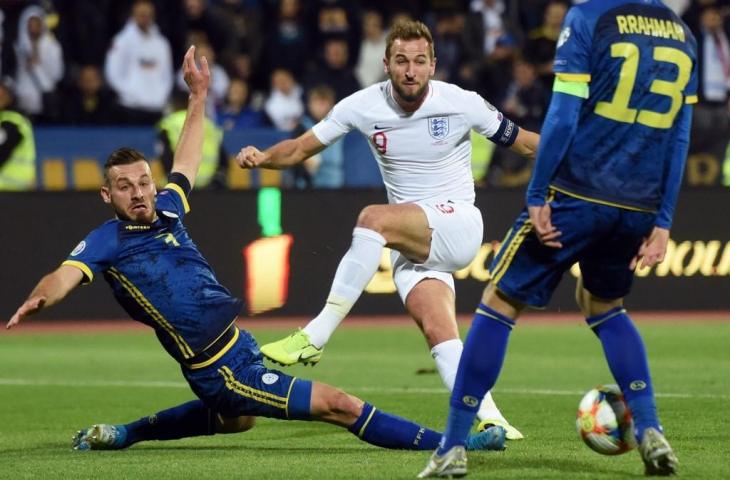 Penyerang Timnas Inggris, Harry Kane melepaskan tembakan saat dihadang dua pemain Kosovo, Senin (18/11/2019). Pada laga Kualifikasi Piala Eropa 2020 tersebut skuat The Three Lions pesta gol 4-0. [ROBERT ATANASOVSKI / AFP]