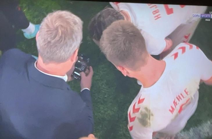 Salah satu staf pelatih Denmark terlihat sedang memeriksa skor pertandingan Belgia dengan Finlandia lewat ponsel, sementara para pemain melihat sambil membentuk lingkaran di tengah lapangan. (Twitter/@AFCDido).