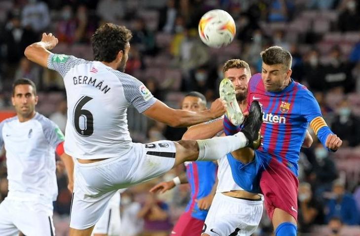 Pemain Barcelona, Gerard Pique dihadang pemain Granada di laga lanjutan Liga Spanyol, Senin (20/9/2021). (AFP/LLuis Gene)