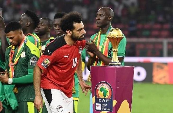 Penyerang Timnas Mesir, Mohamed Salah berjalan melewati trofi setelah kalah dalam pertandingan final Piala Afrika 2021 lawan Senegal di Stade d'Olembe, Yaounde, Kamerun. (Kenzo TRIBOUILLARD/AFP)