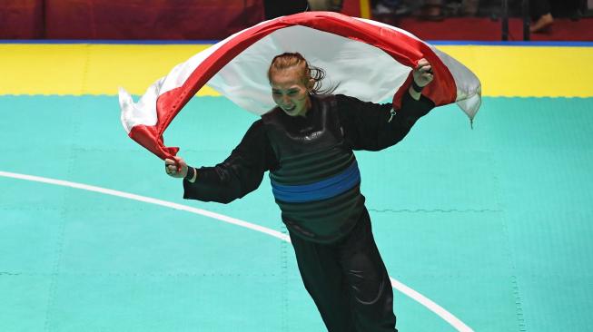 Selebrasi pesilat Indonesia, Wewey Wita, membawa bendera Merah Putih usai mengalahkan pesilat Vietnam, Thi Them Tran, dalam babak final Kelas B Putri Asian Games 2018 di Padepokan Pencak Silat, Taman Mini, Jakarta, Rabu (29/8). [Antara/INASGOC/Melvinas Priananda]