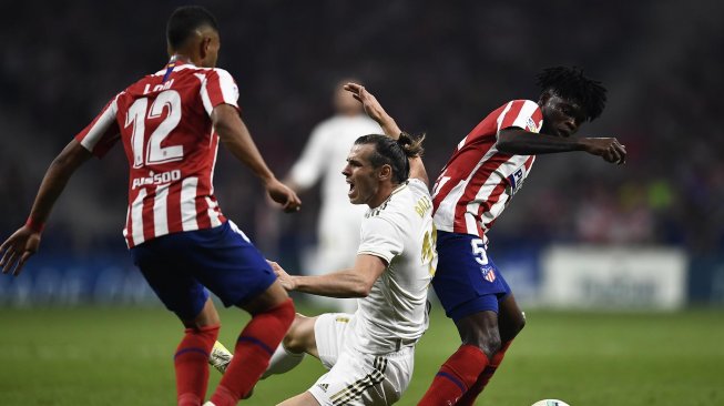 Gelandang Atletico Madrid, Thomas Partey (kanan) dan bek Atletico Madrid, Renan Lodi (kiri), menghalau pemain depan Real Madrid, Gareth Bale selama pertandingan sepak bola liga Spanyol antara Atletico Madrid melawan Real Madrid di stadion Wanda Metropolitano, Madrid, Spanyol, Minggu (29/9) dini hari WIB. [OSCAR DEL POZO / AFP]