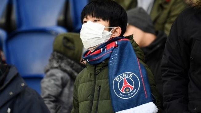 Suporter Paris Saint-Germain (PSG) memakai masker meyusul merebaknya virus corona saat menyaksikan laga melawan Dijon pada laga lanjutan Ligue 1 di Parc des Princes stadium, Paris. FRANCK FIFE / AFP