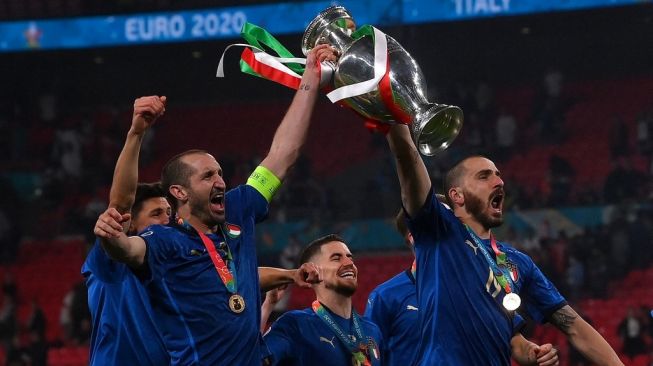 Duo bek andalan Timnas Italia, Giorgio Chiellini (kiri) dan Leonardo Bonucci mengangkat trofi usai timnya menjadi juara Euro 2020, pasca mengalahkan Inggris pada laga final di Wembley, London, Senin (12/7/2021) pagi WIB. [Laurence Griffiths / POOL / AFP]